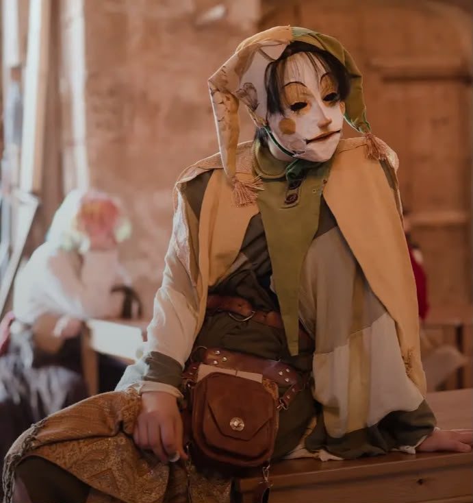 Handmade costume of layered linen with a painted white mask, hood and leather satchel