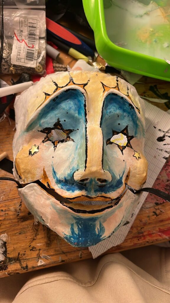 Broad-grinning mask with blue-rimmed eyes and star-shaped eye holes
