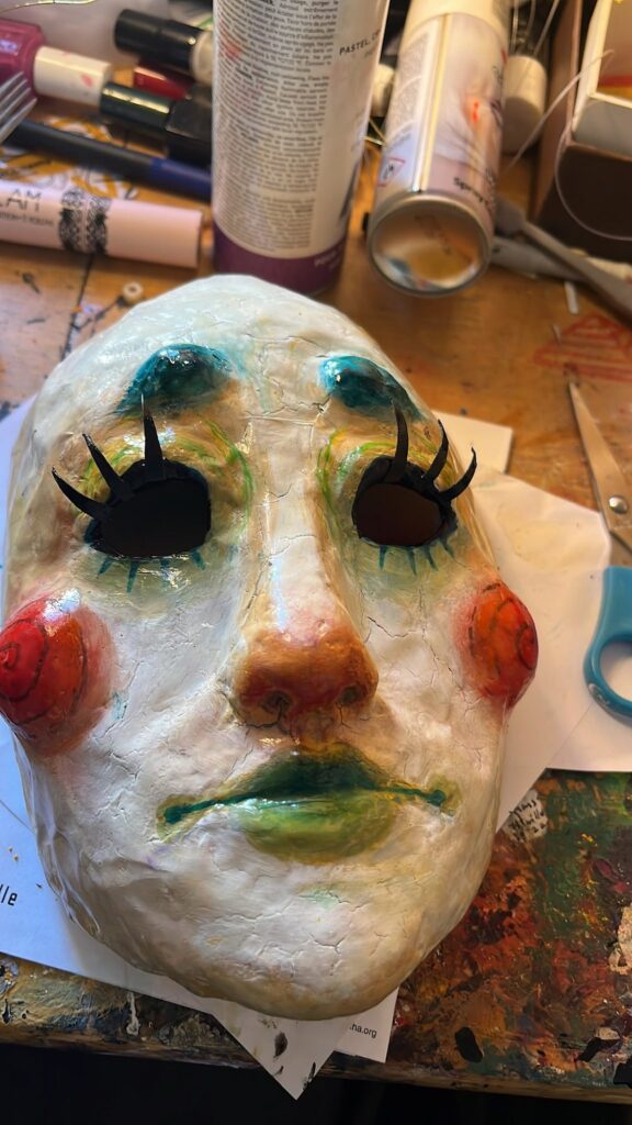 Pale mask with long painted lashes, red cheeks and a red nose