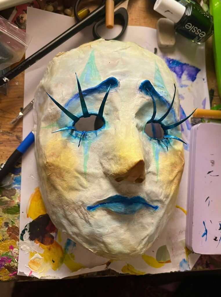 Mask with turquoise lashes and brows on a cream face with blue lips
