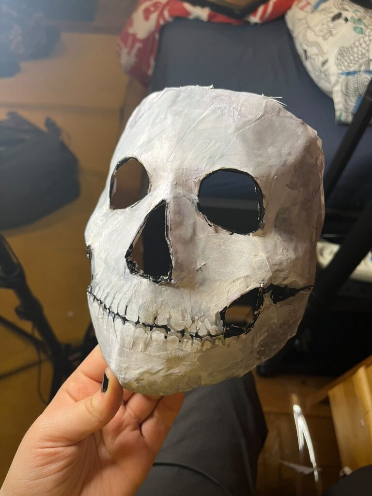 Raw white skull mask with a stitched mouth, held in one hand