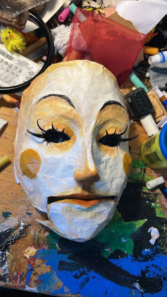 Mask with heavy lashes, gold cheek spots and an orange mouth